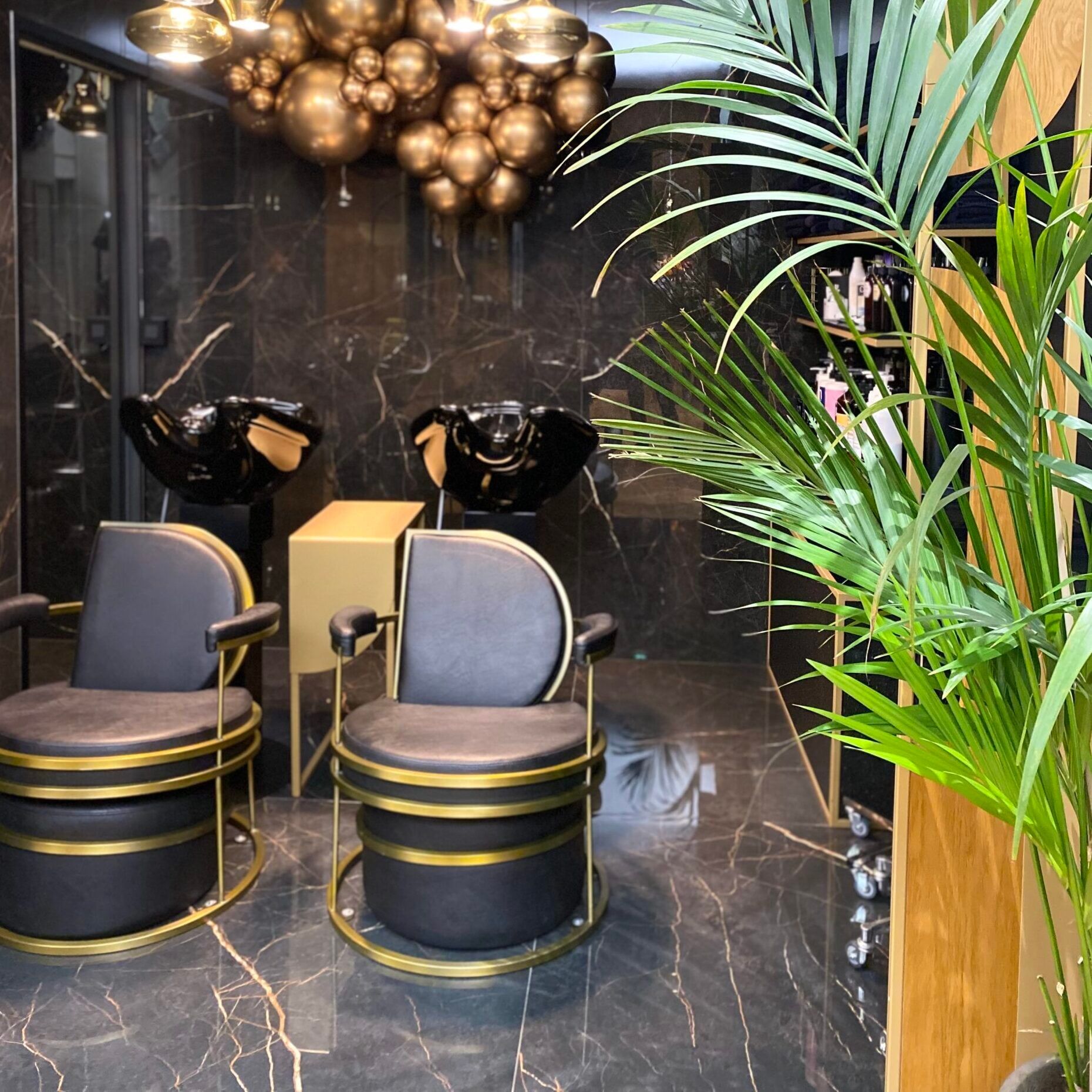 Bacs à shampoing devant un mur en marbre noir, sous un lustre de sphères dorées, au salon du Vieux-Lille