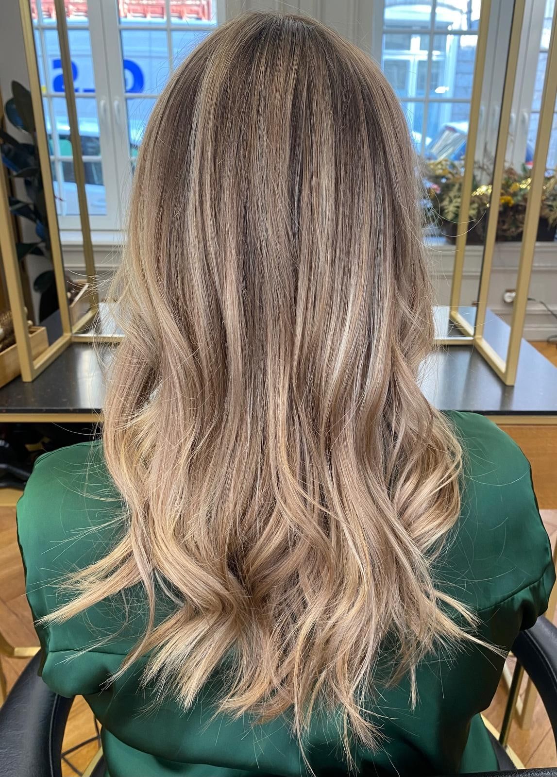 Balayage blond beige sur cheveux longs ondulés, vu de dos devant les miroirs en laiton du salon Maison de Coiffure Eva, Vieux-Lille