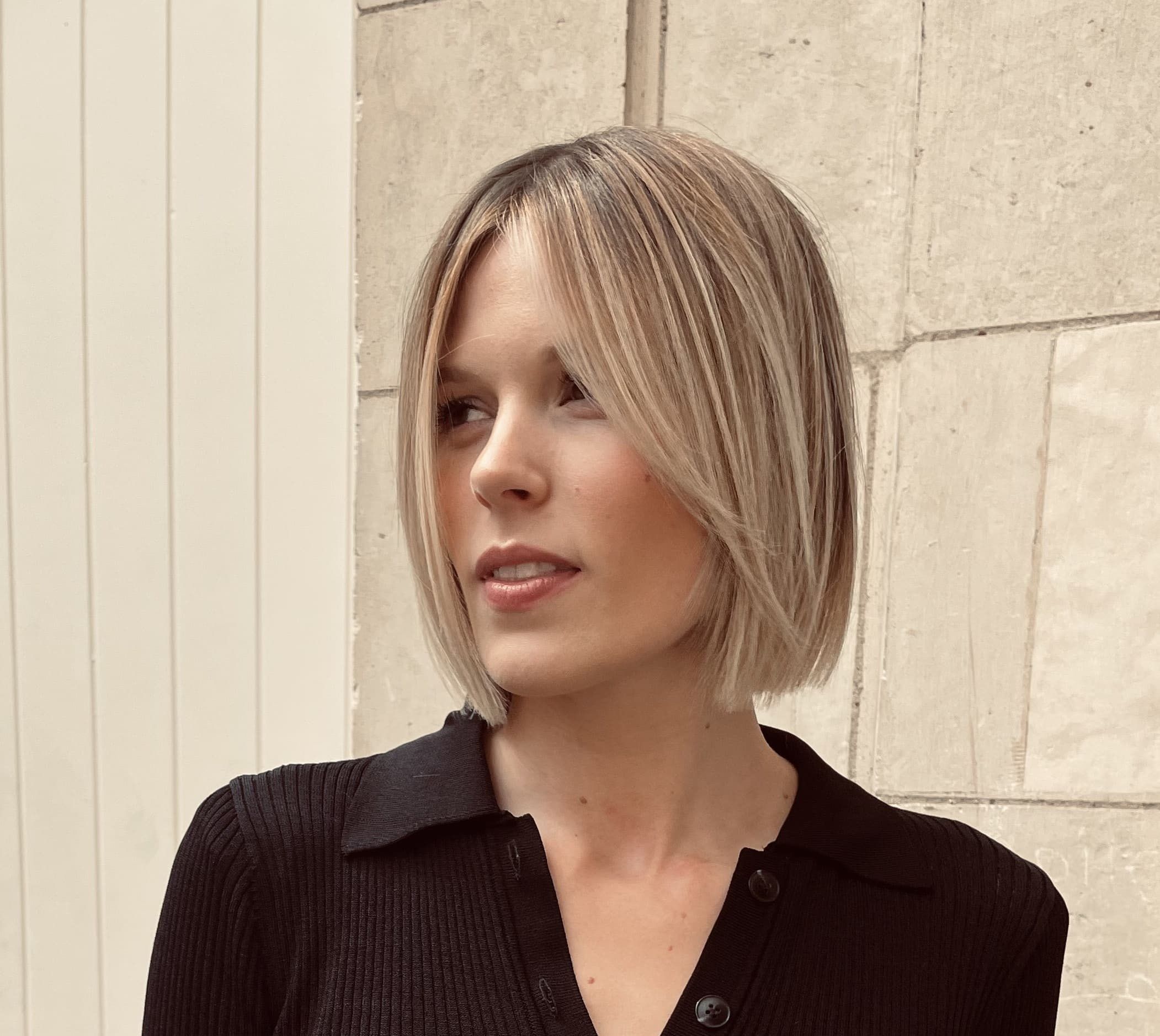 Carré lisse au menton, blond beige sur racine foncée, avec une frange rideau qui encadre le visage