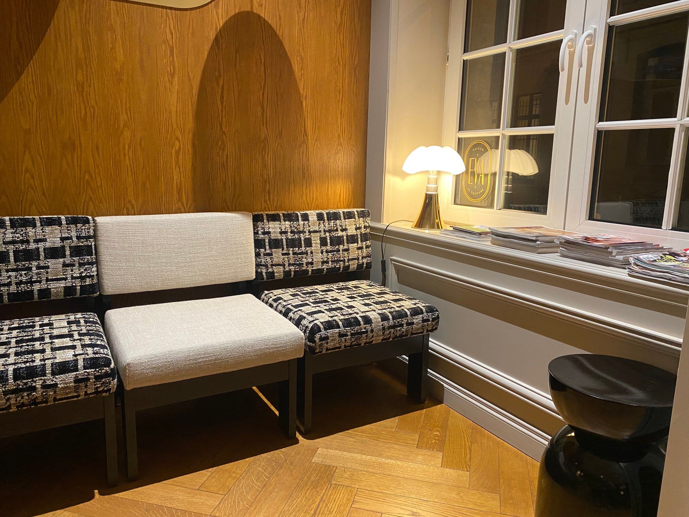 Coin d'attente avec fauteuils en tweed noir et blanc, lampe champignon dorée et magazines posés sur le rebord de fenêtre