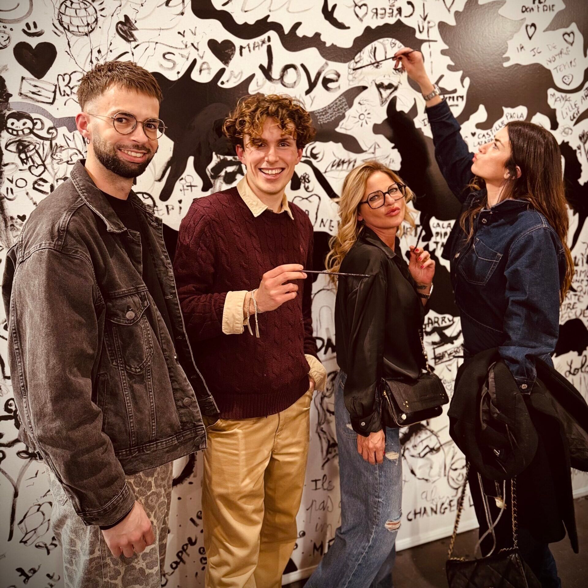 Quatre membres de l'équipe Maison de Coiffure Eva, souriants devant une fresque noir et blanc