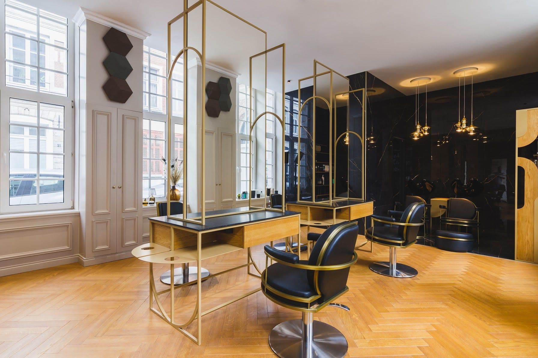 Intérieur du salon Maison de Coiffure Eva dans le Vieux-Lille : parquet à chevrons, coiffeuses à miroirs encadrés de laiton et fauteuils en cuir noir